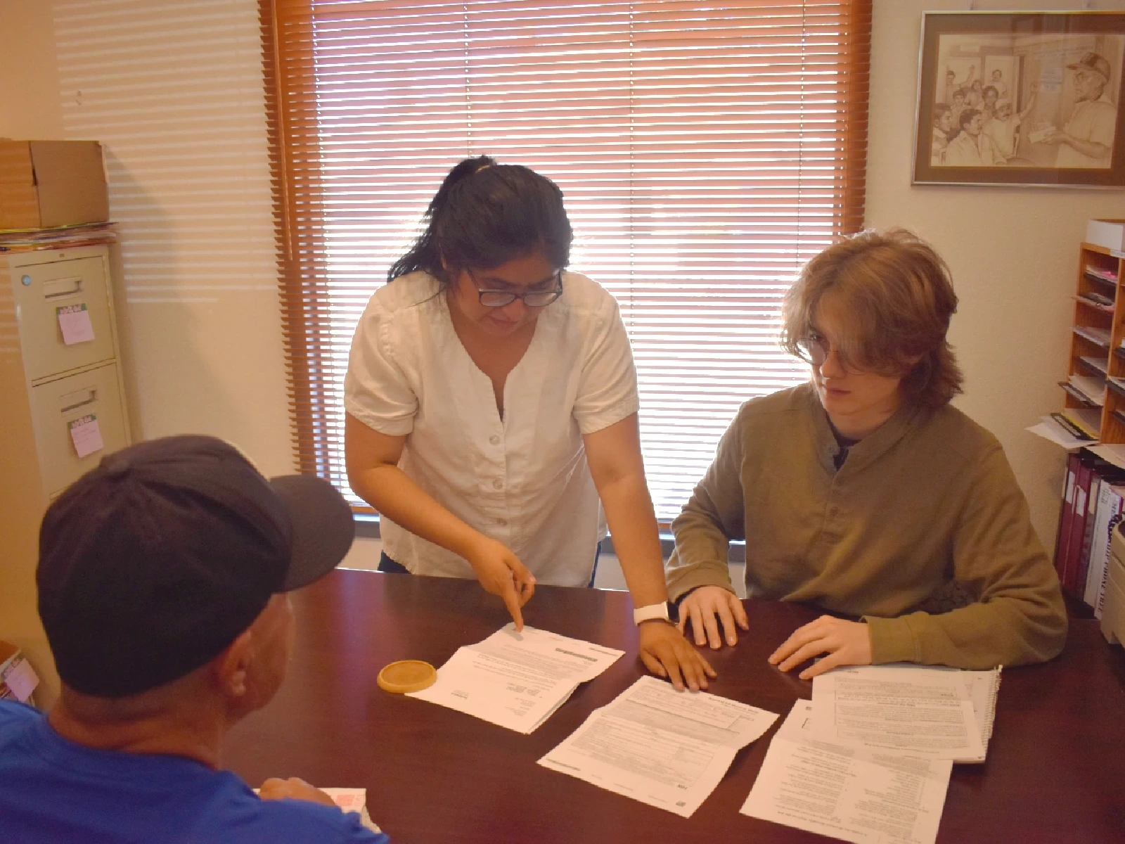 A young woman provides training to a young man on an advocacy session in an office setting