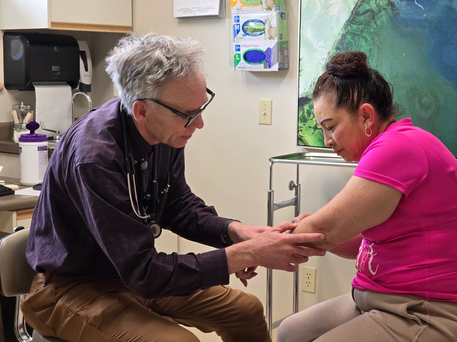 A doctor examines the left arm of a patient in a medical office