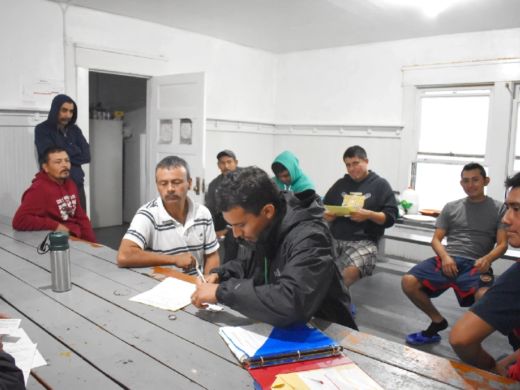 A volunteer signs up a room full of farm workers as members as they are sitting in a dining room