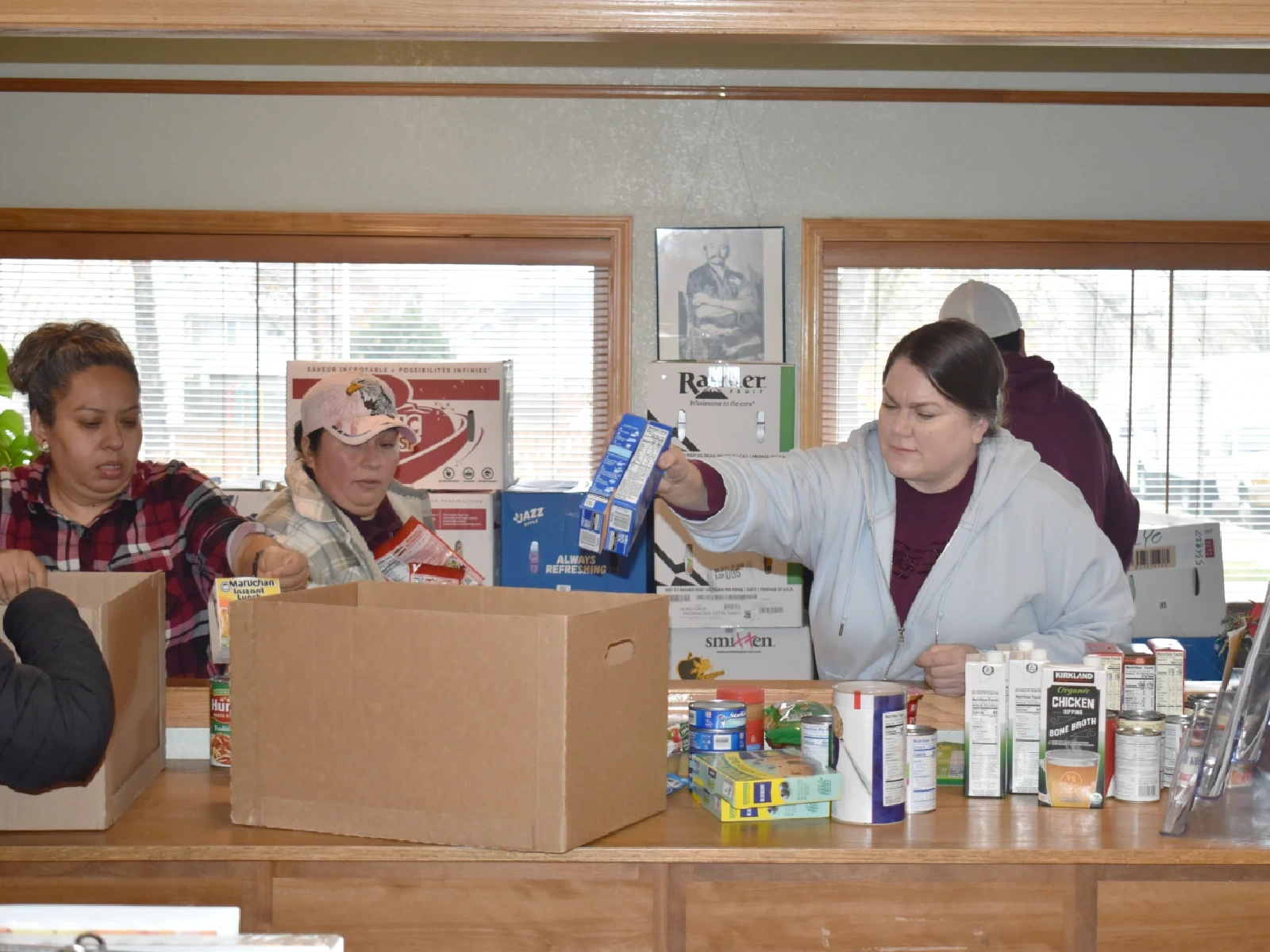 Three women work together to fill boxes with non-perishable food items for distribution.