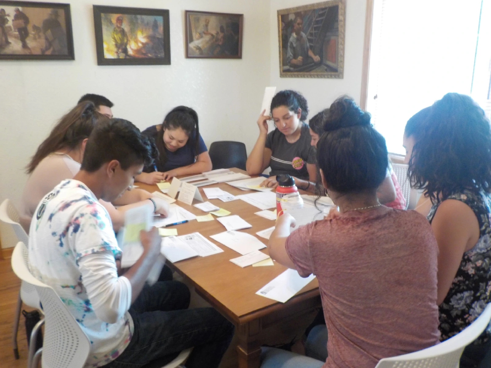 A group of high school students work together to mail out letters in a room with beautiful paintings on the wall.