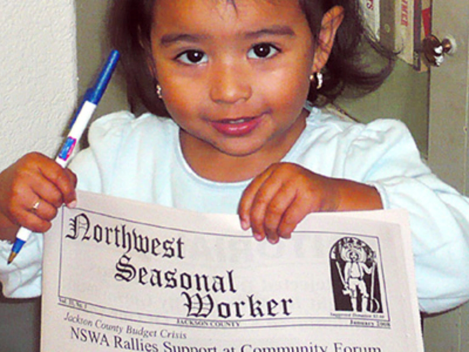 A girl holds up a copy of the Northwest Seasonal Worker newsletter