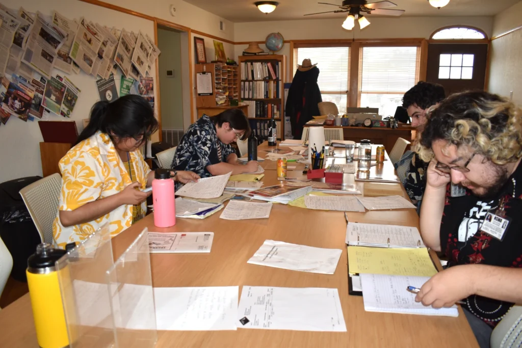 Four people sit at a long table and each are making phone calls